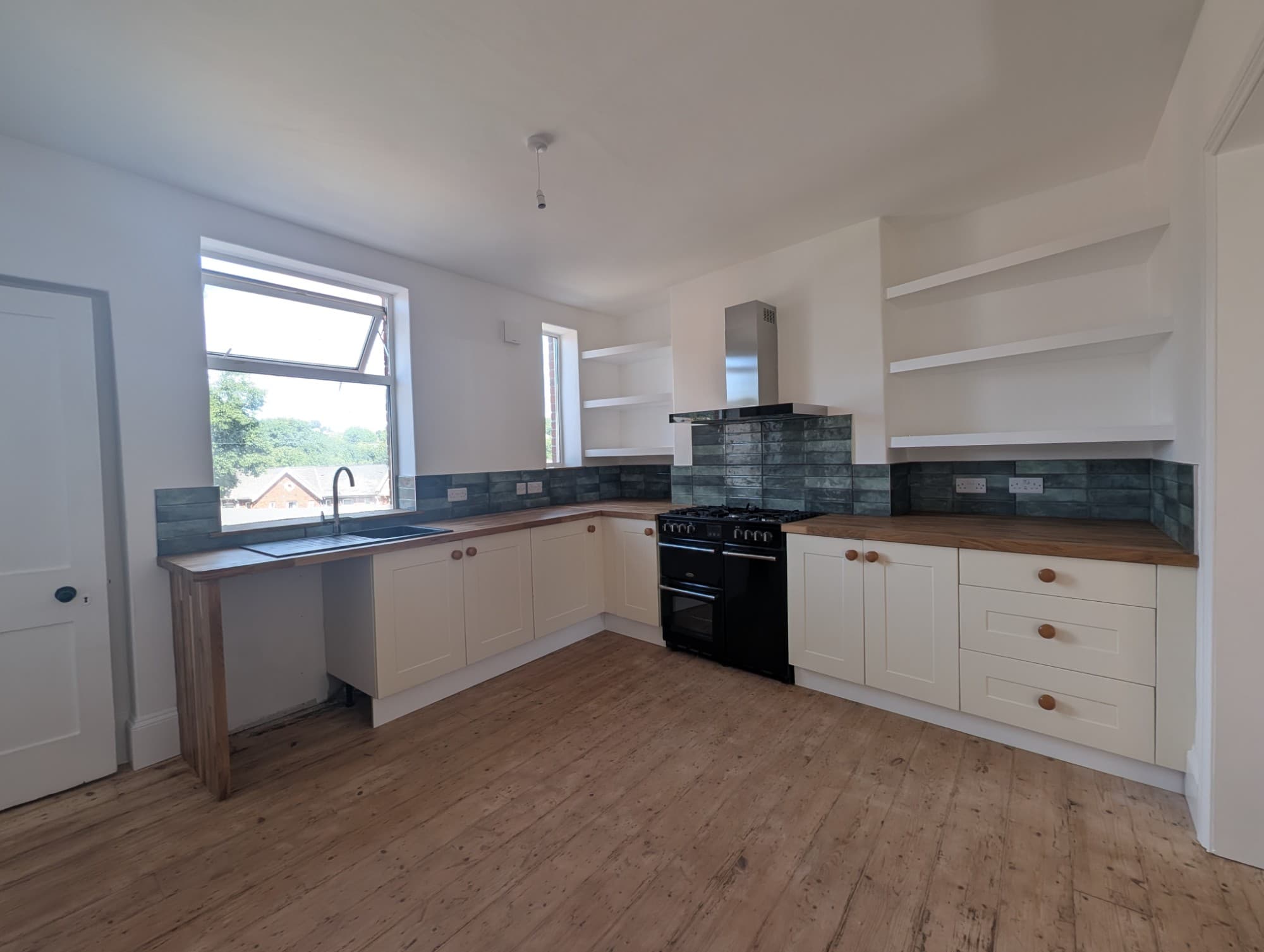 Newly fitted kitchen with cream shaker units, oak worktops and a green feature tile splashback