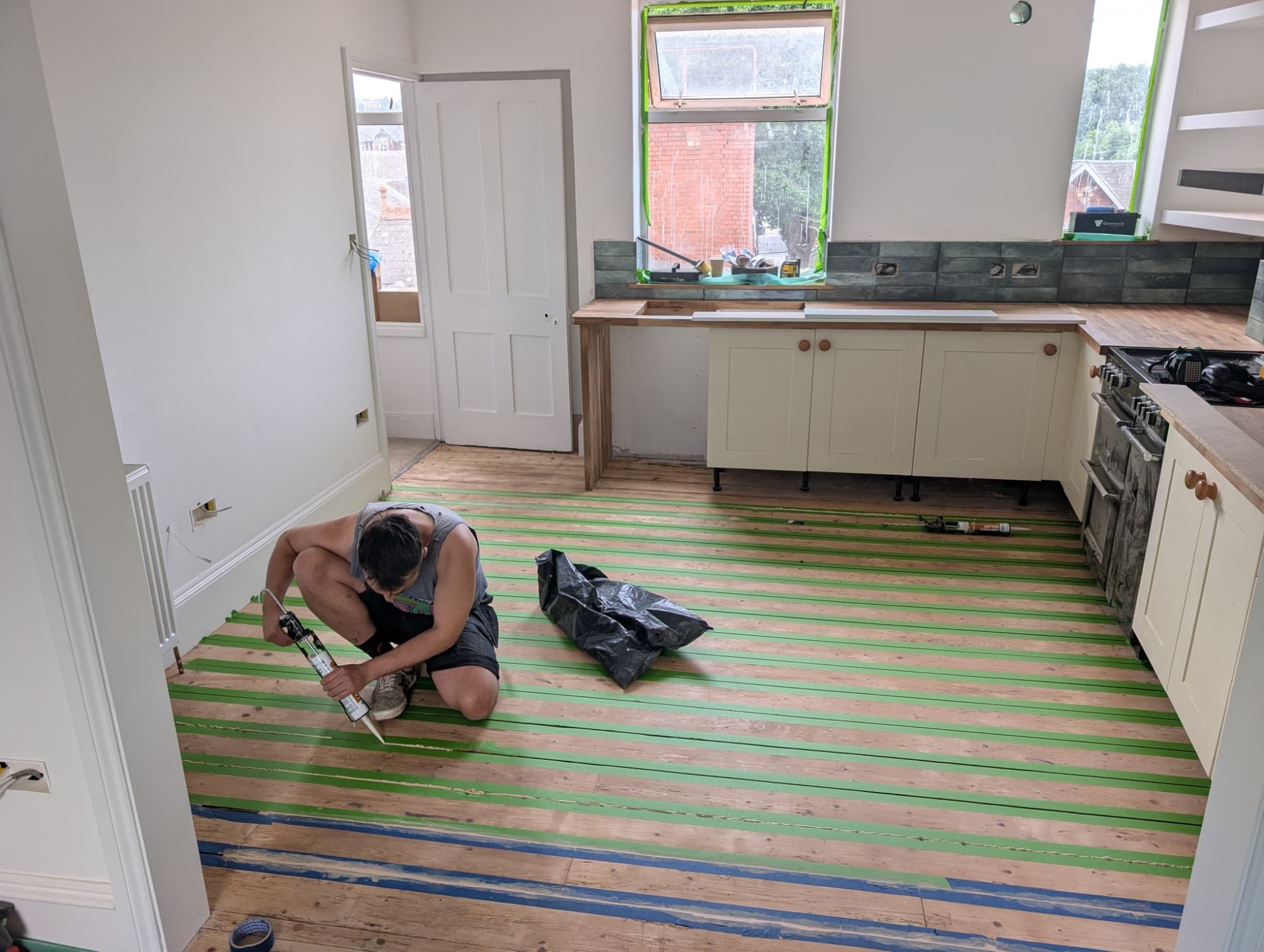 Kitchen floorboards being prepared with masking tape and floor filler ahead of finishing