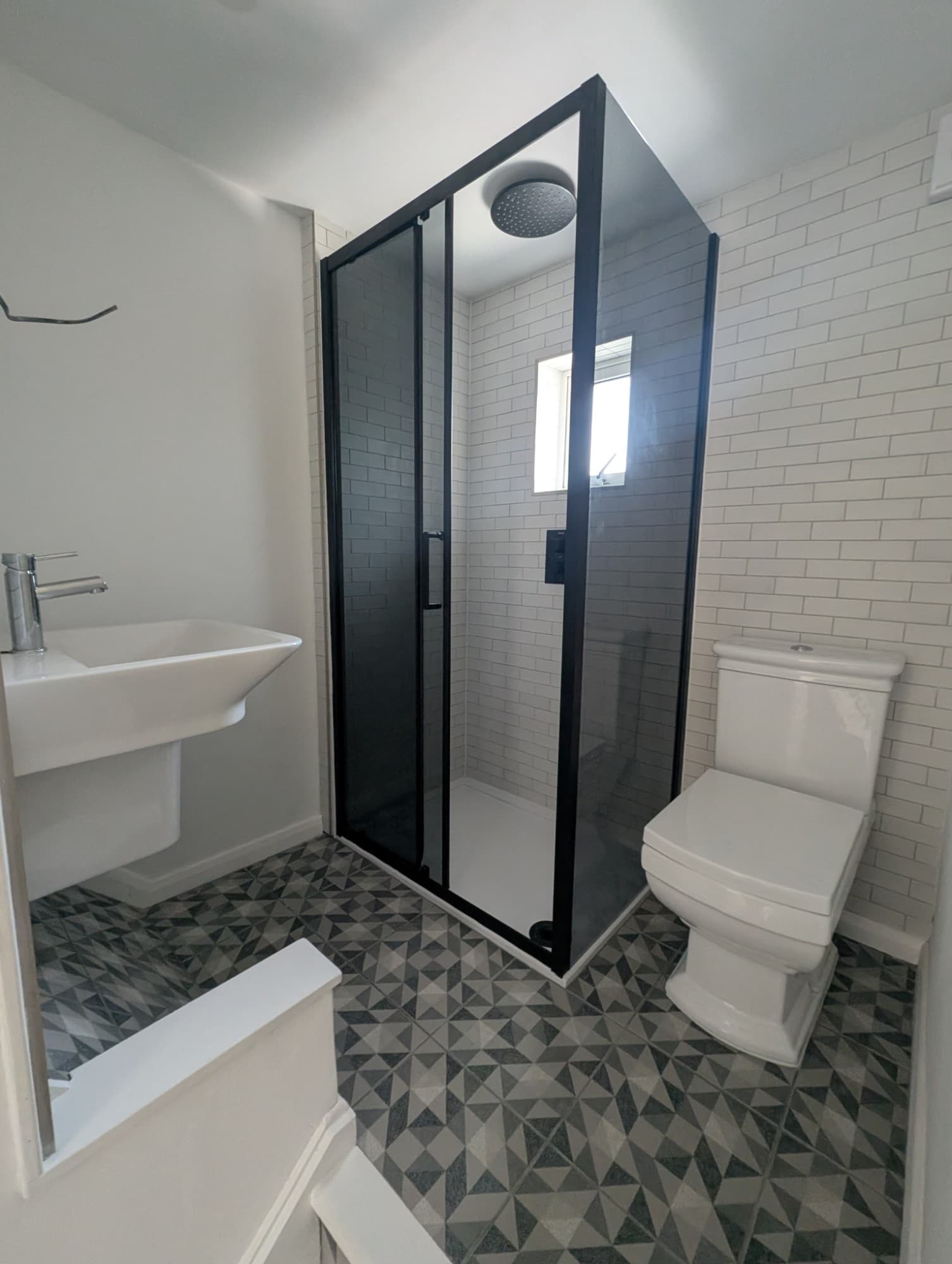 Compact bathroom refit with black-framed shower enclosure, white subway tile walls and geometric grey floor tile